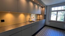 modern kitchen with stainless steel countertops, tiled backsplash, under-cabinet lighting, double sink, gas stove, and a window with a view
