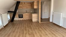 An empty kitchen area with wooden floor, wooden kitchen cabinets, integrated oven and extractor, gas stove, and white radiators on both sides