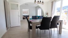 Dining room with a table and chairs, white walls, tiled floor, large windows, and a view of the outside