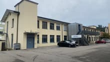 Two-story building, light yellow facade, blue double doors, windows, cars parked in front