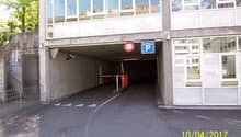 The image shows the entrance to an underground parking garage. The entrance is marked with a parking sign and has a height limit of 2 meters. The garage appears to be located in a commercial or office building, with large glass windows on the upper floors