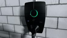 Black electric vehicle charging station with a green LED ring light, mounted on a concrete wall