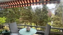 Balcony with a table, chairs, and a canopy, overlooking a grassy field and trees
