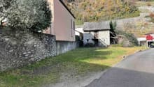 2 buildings, grassy area, stone wall, hill in background