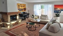 Fireplace, piano, two sofas, coffee tables, rug, paintings, lamp, plant
