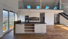 Open kitchen with central island and modern appliances, large windows, wooden floor, balcony, and a high ceiling