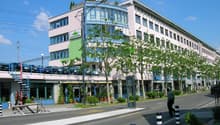 A multi-story building with a rooftop terrace, multiple windows, and a car parking area on the first floor.