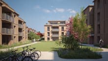 Modern apartment buildings with balconies, landscaped area with trees, a green lawn, and a paved pathway for bicycles