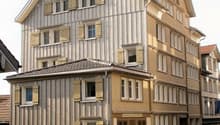 3 story building, wooden exterior, multiple windows, brown doors, cobblestone street