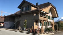 two-story chalet, wooden exterior, green shutters, balconies, surrounded by plants and rocks, mountain in the background