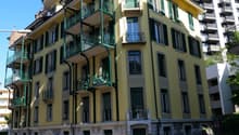 large yellow building with green accents, 4 balconies, multiple cars parked in front