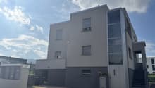 Modern apartment building, glass windows, grey walls, entrance door, small garden