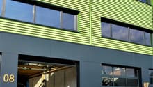 Industrial-style building, green exterior, multiple glass windows, car in the garage