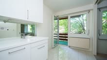 ein modernes Badezimmer mit weißen Schränken, einem großen Fenster und einer Glasschiebetür zu einem anderen Raum / a modern bathroom with white cabinets, a large window and a sliding glass door t
