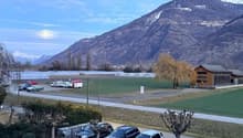 Parking lot with multiple cars parked, mountains in the background, and a building on the right side