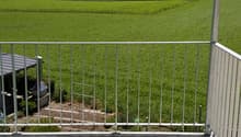 balcony with white railings, floor, open view of field, some trees