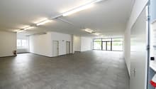 Wide open space, concrete floor, two doors, fire extinguisher, glass walls, white walls, ceiling lights