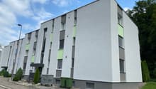 Modern apartment building with gray and green exterior, multiple windows, and a flat roof.