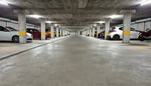 Underground parking garage with concrete ceiling and columns, lined with parked cars on both sides