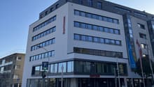 Commercial building, large windows, glass doors, 5 stories, blue sign, flags, banners