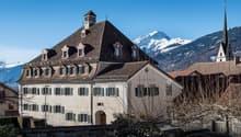 large building with multiple windows, brown roof, stone walls, surrounded by mountains