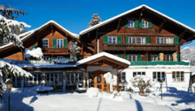 2 story brown wooden house, green windows, snow covered, balcony on the first floor