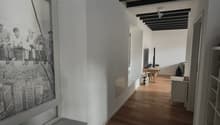 Empty hallway with wooden floor, white walls, black beams, large window with a picture, small table with TV, white shelves