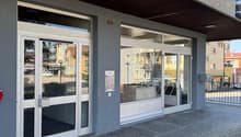 Exterior of a building with glass doors and windows, concrete floor, metal railings, and a small signboard.