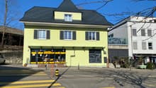3 story building, yellow exterior, black roof, glass doors, windows, street view
