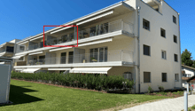 White apartment building, multiple balconies, well-maintained garden, paved walkway