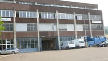 large office building, brown color, many windows, large entrance, trucks and cars parked in front