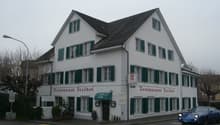 2-story restaurant building, white exterior, green shutters, red text sign, shrubs and plants in front, streetlight and blue car in the background