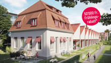 A row of white houses with brown roofs, each with multiple windows and awnings, a pathway in front, and a bicycle parked nearby.