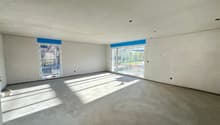 Empty room, white walls, gray floor, two large windows, bright daylight