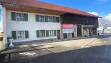 White and brown building, terracotta roof, multiple windows, two doors, sign indicating it is for sale