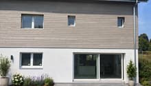 2 story house, wooden and white exterior, solar panels on roof, large glass doors, garden with plants