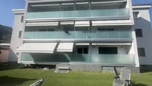 3-story modern apartment building with glass balconies, white exterior, and a grassy lawn in front