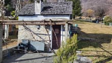 Stone house with chimney, brown door, stone pathway, wooden fence, grassy area, tree, plants, distant mountain