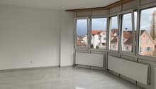 Spacious living room with large windows offering a view of the surrounding buildings, hardwood floors, and a modern, minimalist design.
