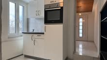modern kitchen with white cabinets, black countertop, built-in oven, sink, and faucet, white tiled floor, window with view
