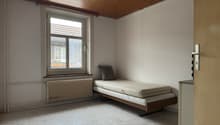 Empty room with a single bed, a window, a radiator, and a wooden ceiling.