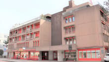 Multi-story commercial building with red accents, balconies, and retail spaces on the ground floor