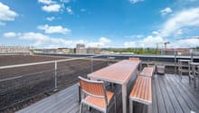 Outdoor wooden deck, dining table and chairs, metal railings, plants in pots, city skyline view