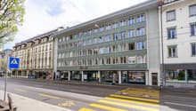 Multi-story building, green facade, glass windows, shops on the ground floor, bicycle parking sign