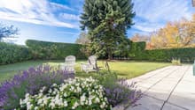 well-maintained garden with lawn, shrubs, and two white chairs