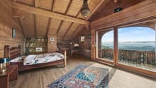 bedroom with wooden bed, rug, wooden wall and flooring, large window with wooden balcony, lamps, desk, bookshelves