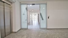 Empty hallway with gray tiles, glass doors, and ceiling lights