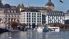 Urban waterfront with buildings, Credit Suisse logo, water, docked boats, people, flags