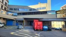 modern building with glass walls, raised ground floor,  blue entrance doors, cars parked in front