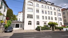 4 story building, white exterior, multiple windows, car parked in front, street with tram tracks
